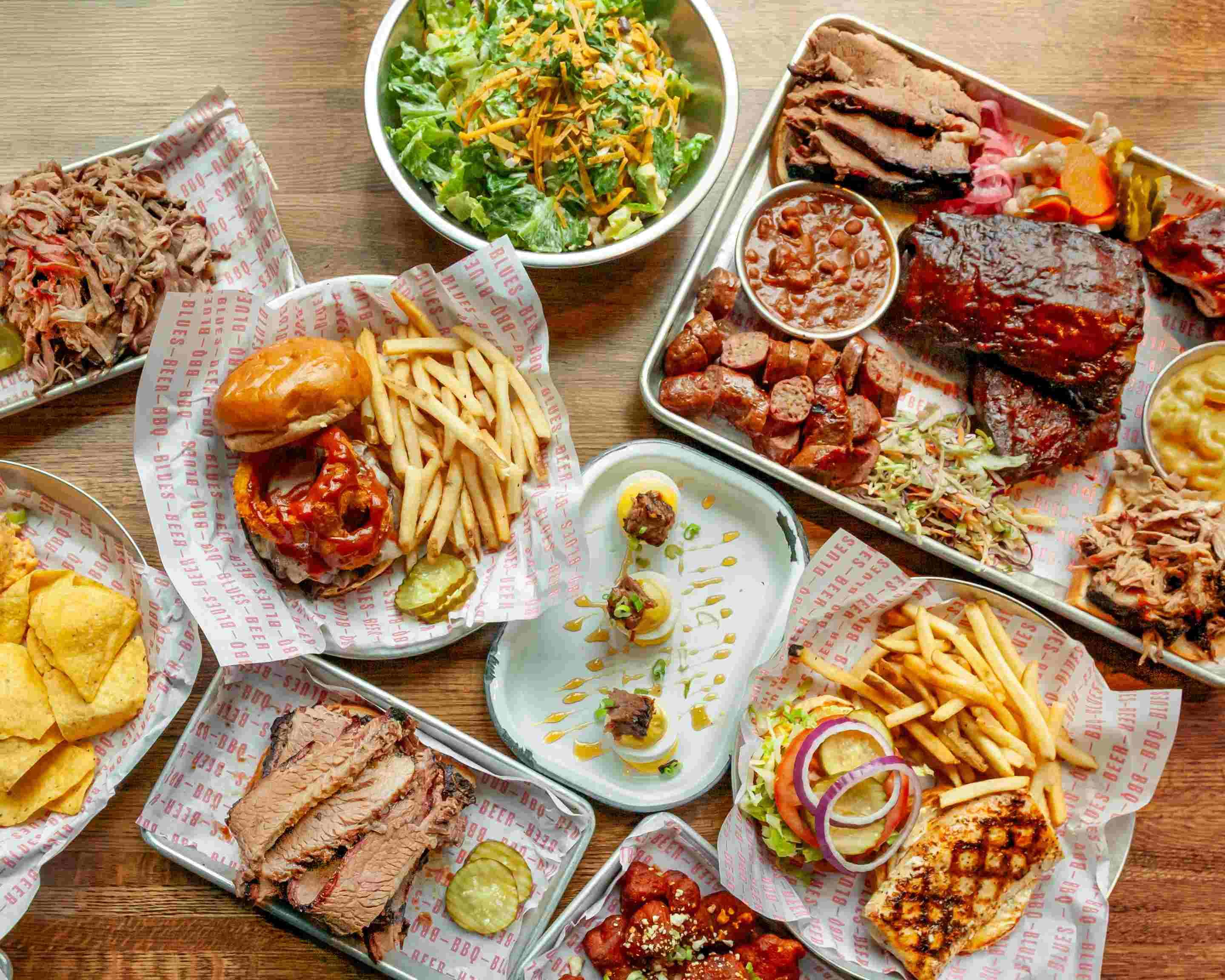 A full table spread of BBQ items, including ribs, pulled pork, sandwiches, salads, and sides.