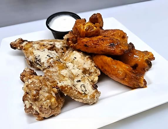 Plate of chicken wings, some plain and some sauced, with a side of dipping sauce.
