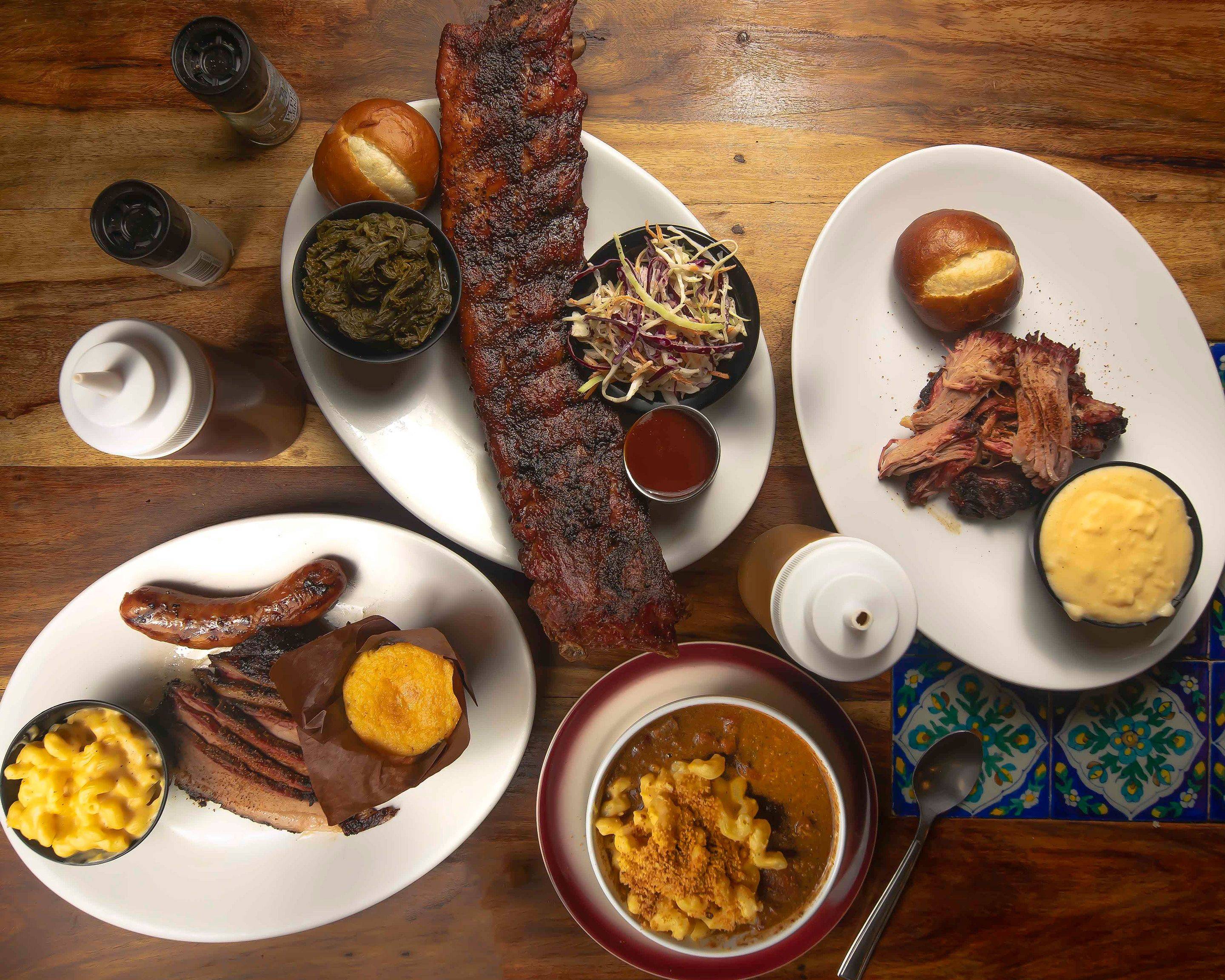 An overhead shot of a variety of BBQ dishes including ribs, brisket, sausage, mac and cheese, collard greens, and coleslaw.