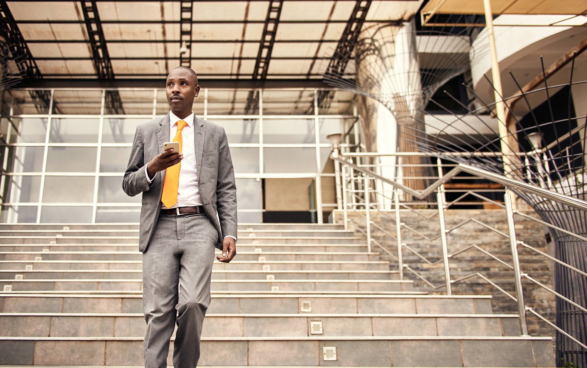 Businessman walks down staircase holding his phone in front of him.