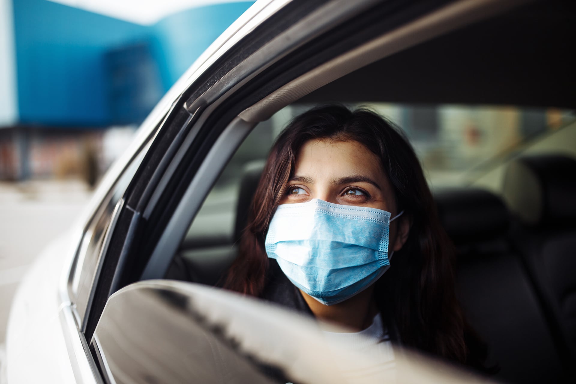 Woman sitting in the back seat of a white car looks out a partially open car window.